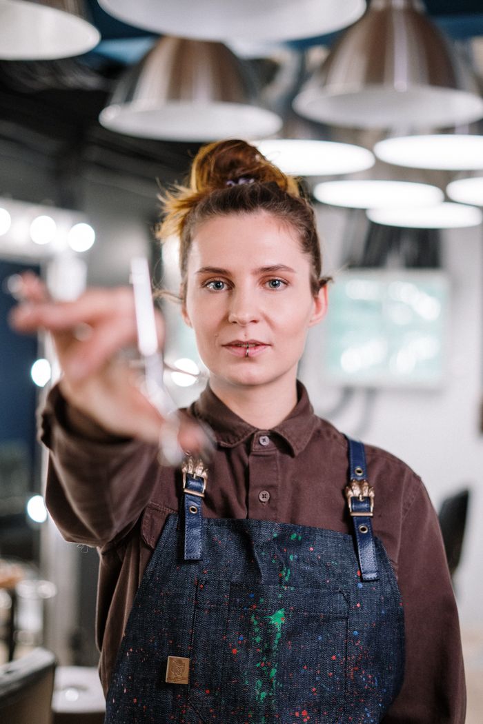 service-01 Portrait of a female hairstylist holding scissors in a modern salon setting, showcasing professional haircare.